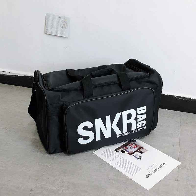 Black duffel bag with 'SNKR' branding on a concrete floor.