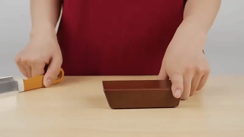 Person holding a small brown knife sharpener on a light wooden surface.
